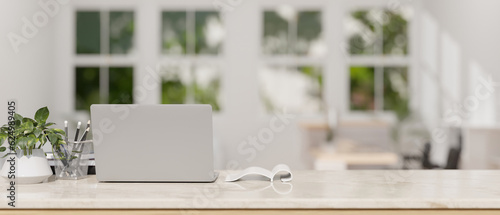 Back view of a workspace with laptop on a white marble tabletop in modern white room