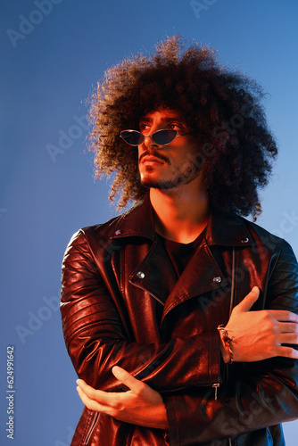 Portrait of a stylish man with curly hair on a blue background multinational, colored light, trendy glasses, modern concept.