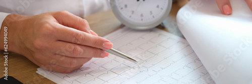 Close-up of female doctor with alarm clock and cardiogram on hospital desk.