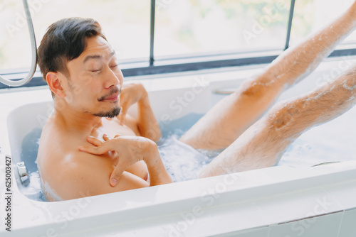 Funny asian man play and pose in a bathtub in the bathroom.