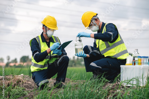 Fototapeta Two Environmental Engineers Inspect Water Quality and Take Water Samples Notes in The Field Near Farmland, Natural Water Sources maybe Contaminated by Toxic Waste or Suspicious Pollution Sites