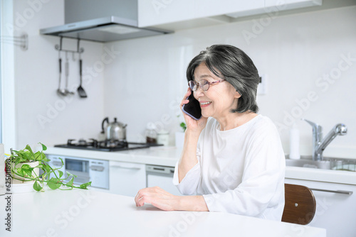 Elderly Asian (Japanese) talking on a cell phone with a smile Background Kitchen