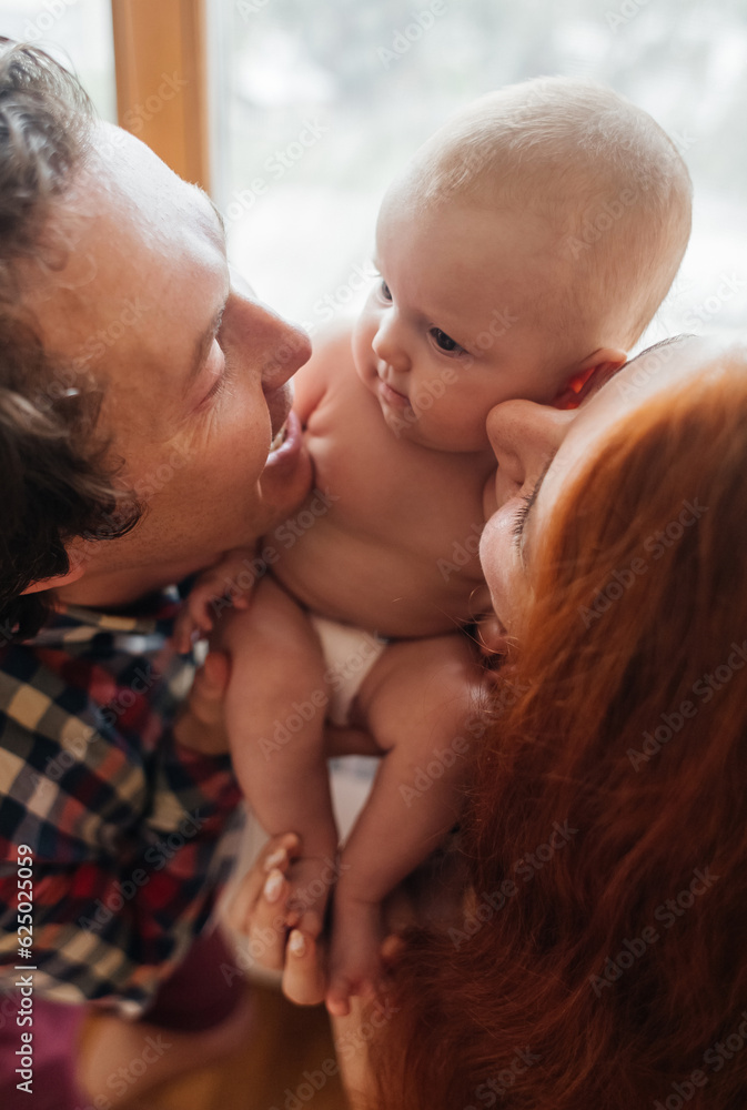 Mom and dad newborn. Caring and loving parents kiss the child on both cheeks. The concept of loving parents, the manifestation of emotions and a responsible attitude towards motherhood and fatherhood Mom and dad newborn. Caring and loving parents kiss the child on both cheeks. The concept of loving parents, the manifestation of emotions and a responsible attitude towards motherhood and fatherhood