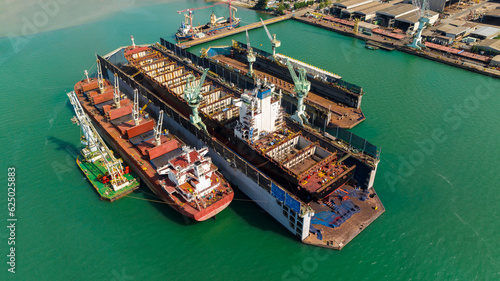 container ship repairing and maintenance on shipyard dry dock in green sea, aerial view