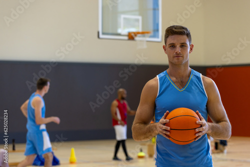 Portrait of diverse male basketball players holding and playing basketball with coach at gym © WavebreakMediaMicro