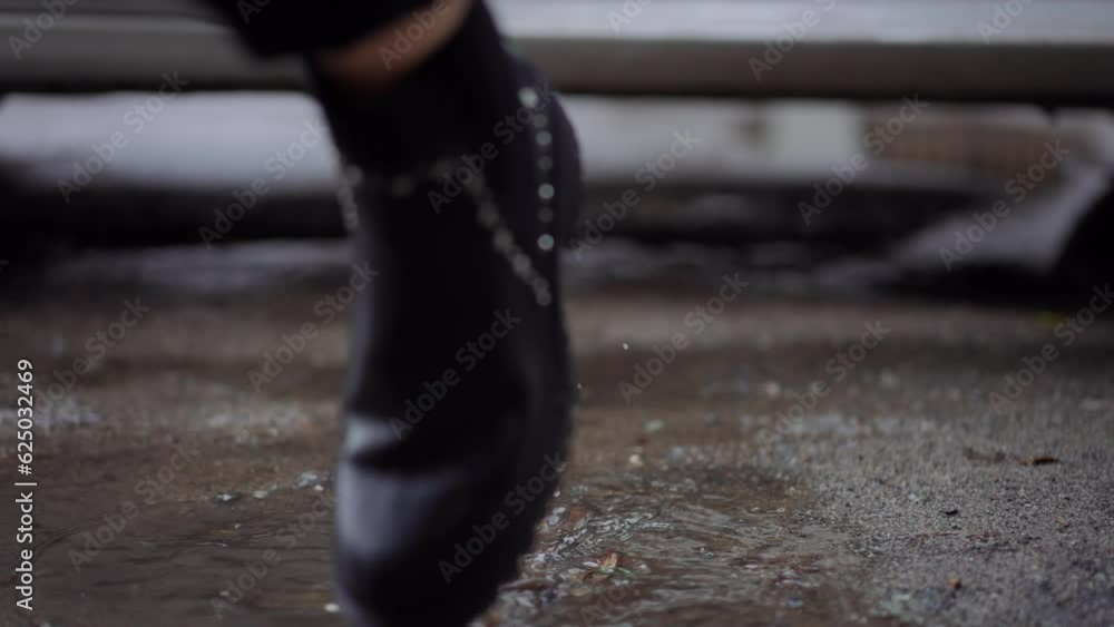 Female feet in leather boots walking out car strolling on puddle leaving. Close-up legs of unrecognizable young confident woman on rainy day outdoors Female feet in leather boots walking out car strolling on puddle leaving. Close-up legs of unrecognizable young confident woman on rainy day outdoors