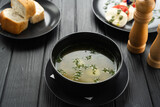 Chicken soup or broth in a bowl on a dark wooden table, restaurant lunch menu, bread on a plate