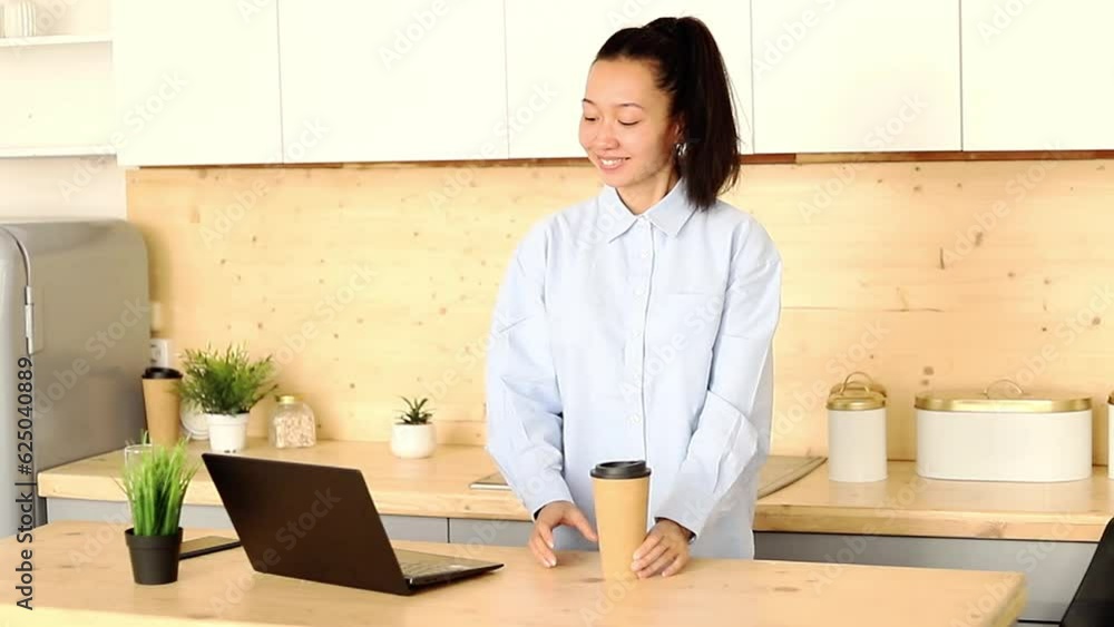 Asian girl works freelance remotely at home in the kitchen sitting at a laptop Asian girl works freelance remotely at home in the kitchen sitting at a laptop