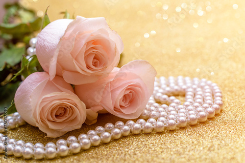 Pink rose and pearl necklace on a shiny gold background 