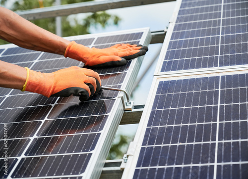 Cropped image of worker installing solar panel on metal beams, tightening with hex key. Renewable and ecological energy. Modern technology and innovation. Man wearing working gloves