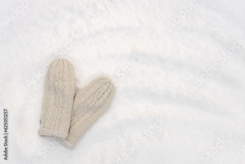 warm knitted mittens on snow, winter background, free space for text