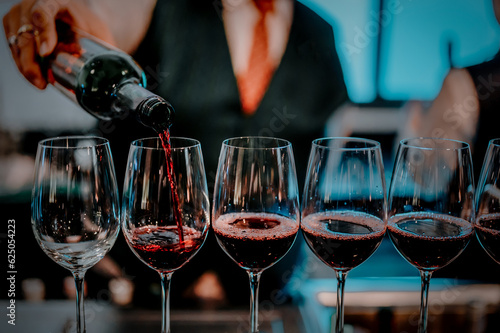 Party and celebration concepts. Bartender pours red wine in glasses at bar. Male sommelier pouring red wine into long-stemmed wineglasses. photo