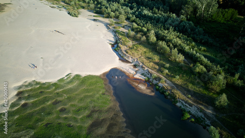 Aerial view of a sandy beach with some green plant, formed as a result of the river drying up during the hot summer, golden hour. 