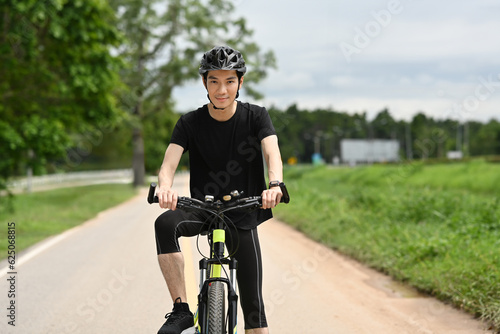 Handsome man cyclist in sport clothes and helmet biking in the public park. Sport, people, outdoors activity and healthy lifestyles © Prathankarnpap