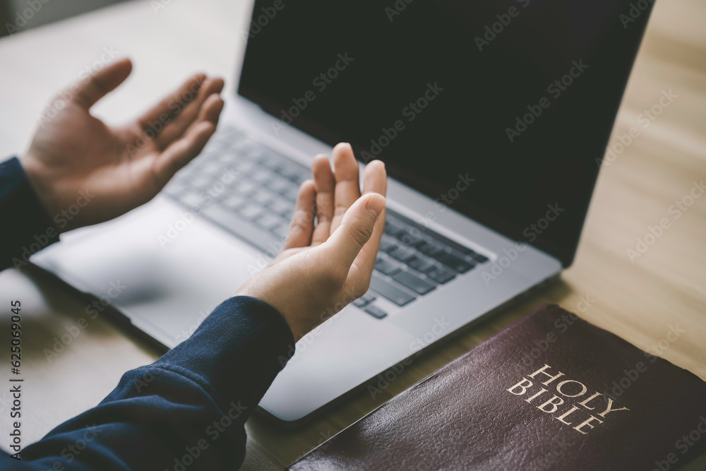 Christian hands folded for prayer with a holy bible and laptop on a wooden table in church for worship online to god in the morning. person pray with faith, Spirituality, and religion concept Christian hands folded for prayer with a holy bible and laptop on a wooden table in church for worship online to god in the morning. person pray with faith, Spirituality, and religion concept