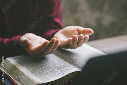 Obraz na plátně Christian hands folded for prayer with a holy bible and laptop on a wooden table in church for worship online to god in the morning