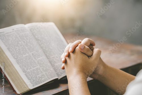 Foto Christian hands folded for prayer with a holy bible on a wooden table in church for worship to god in the morning