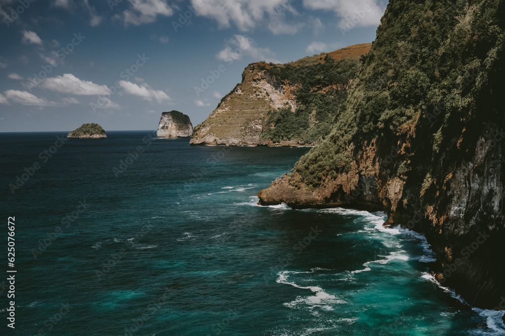 Ocean cliff shore timelapse aerial. Indonesia, Nusa Penida Island. Epic nobody nature scape at sea bay water with dramatic crashing waves at rock on cloudy summer day. Cinematic drone shot