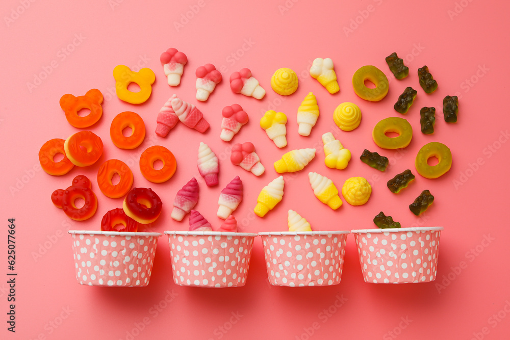 Jelly candies and paper cups on pink background, top view