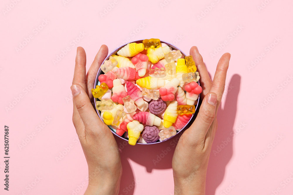 Jelly candies in box and female hands on pink background, top view Jelly candies in box and female hands on pink background, top view