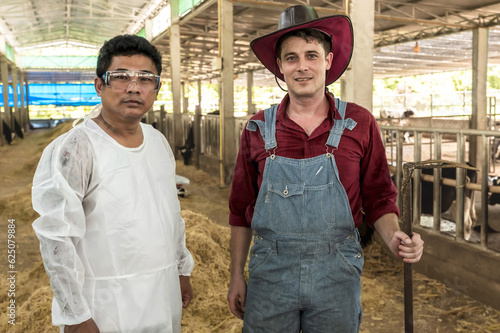 Handsome cowman standing with Asian animal scientist in Dairy Farming photo