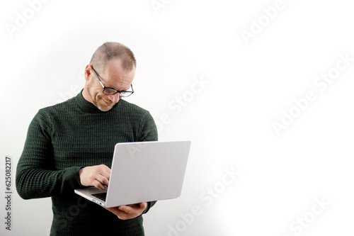 Focused man in glasses using a laptop, typing on the keyboard, writing an email or message, chatting, shopping, a successful freelancer working online on a computer stands on a white background