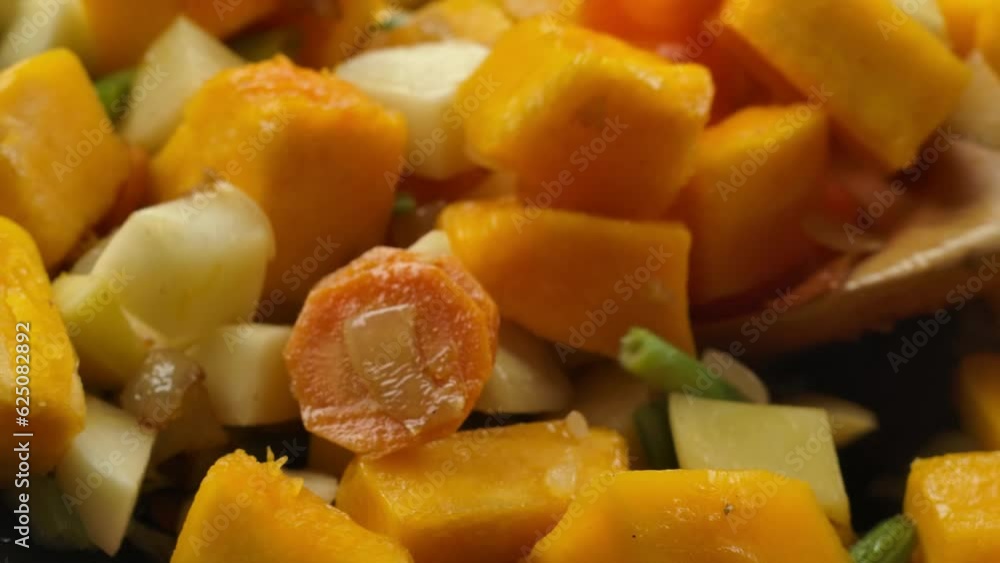Close-up of spoon stirs onions carrots, celery, potatoes and pumpkin in pan Close-up of spoon stirs onions carrots, celery, potatoes and pumpkin in pan