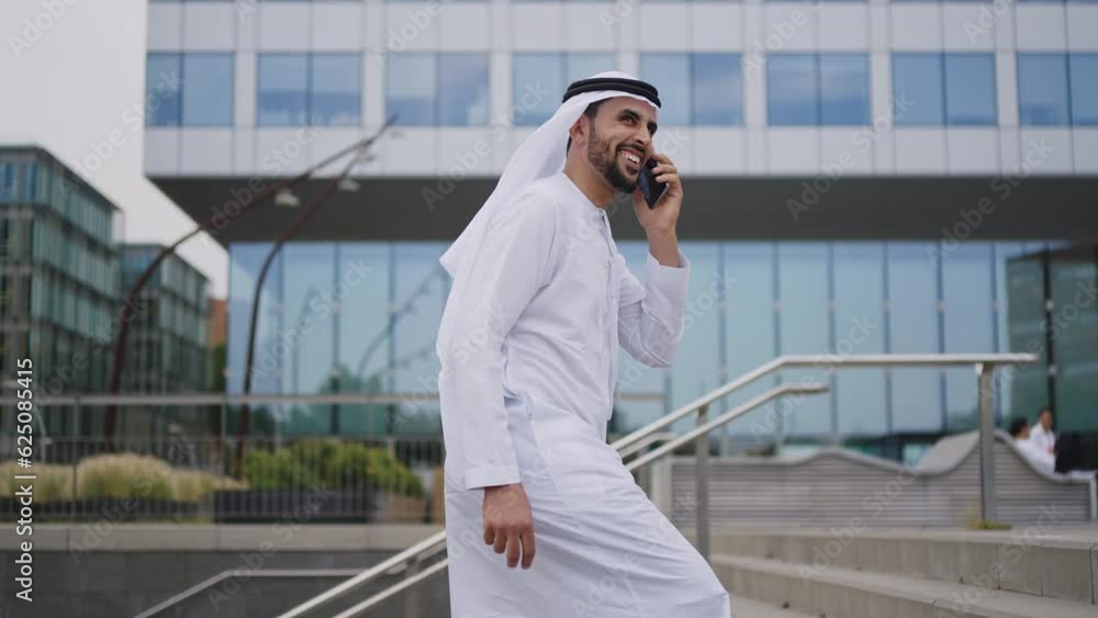 Handsome businessman with the traditional emirates white outfit working outdoor in Dubai city. Concept about middle eastern cultures and business Handsome businessman with the traditional emirates white outfit working outdoor in Dubai city. Concept about middle eastern cultures and business