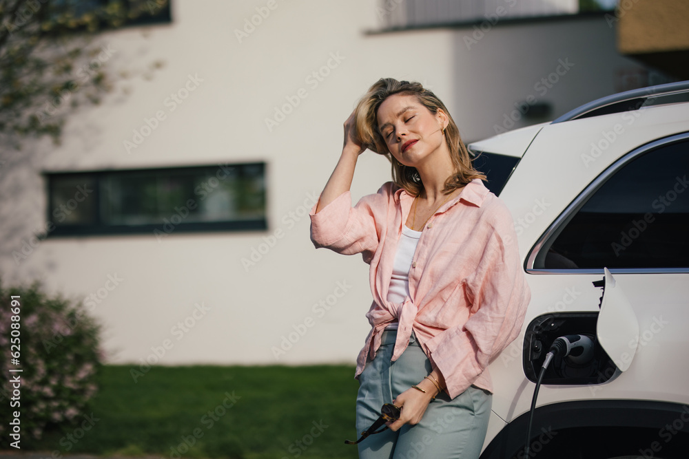 Naklejka premium Young woman charging her electric car in home, sustainable and economic transportation concept.