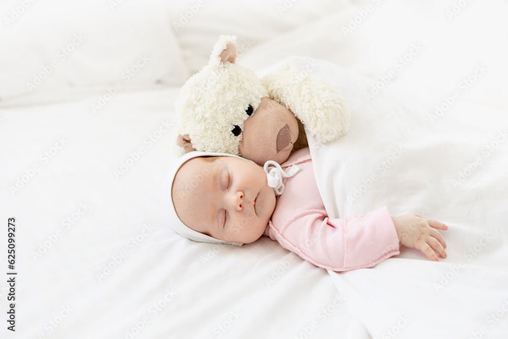 close-up portrait of a small newborn baby girl sleeping on a white cotton bed at home hugging a plush hare under a blanket in a bonnet close-up portrait of a small newborn baby girl sleeping on a white cotton bed at home hugging a plush hare under a blanket in a bonnet