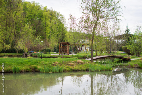 The beautiful view of the park with the trees, green grass field ,gazebo and the pond on background of blue sky. Spring