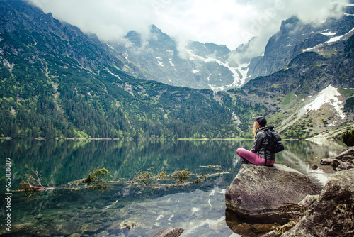 A young girl sitting on a stone by a mountain lake admires the views. Morskie Oko lake, Poland.