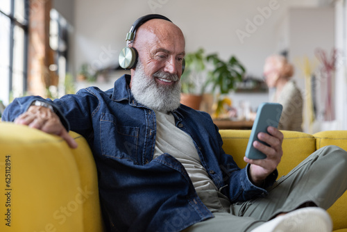 Cool senior man at home using a smartphone with headphones to listen to music