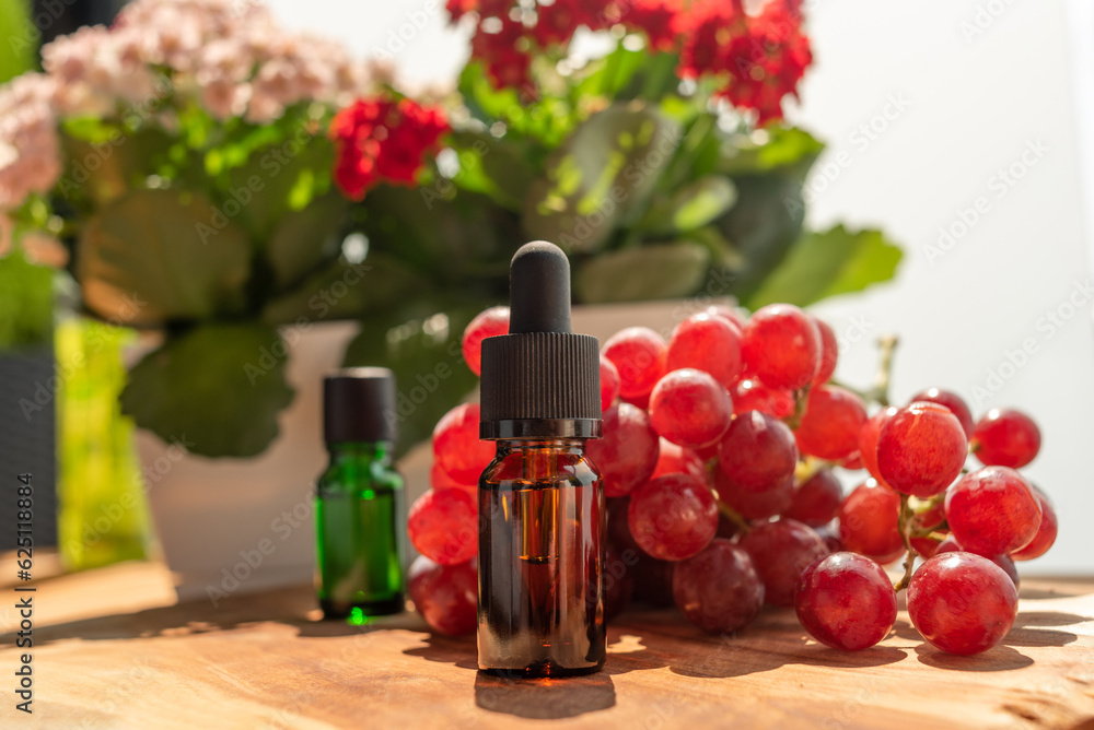 Brown and green bottles of essential oils. natural cosmetics for skin care. Bottles with an eyedropper, grapes and flowers on a wooden table. Taking care of health and beauty.