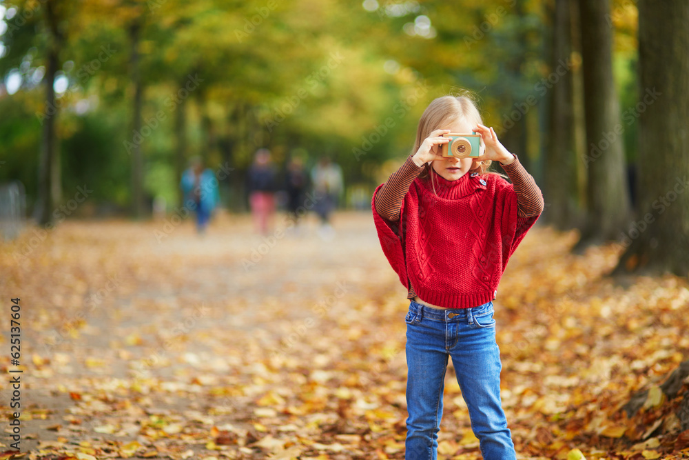 Adorable preschooler girl taking a photo with wooden toy camera in autumn park in Paris, France Adorable preschooler girl taking a photo with wooden toy camera in autumn park in Paris, France