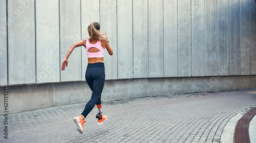 On the way to success.Back view of young disabled woman with leg prosthesis in comfortable sports clothing is running outdoors along the street © Friends Stock