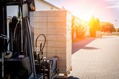 Forklift vehicle manipulating goods in logistic area outside warehouse.