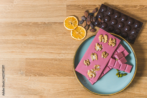 Serving suggestion concept. Brs of ruby aand dark chocolate arrenged on blue plate and wooden table decorated with walnuts slices of orange and cocoa seeds. Copy space. High quality photo