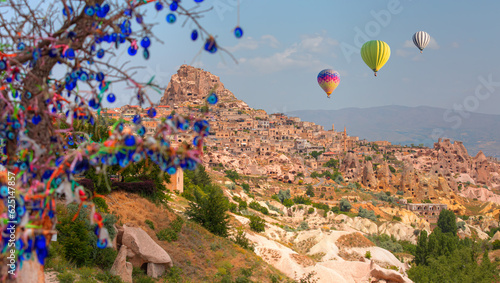 Hot air balloon flying over spectacular Cappadocia - Carved houses in rock and an Nazar (evil eye) tree in Pigeon Valley, Uchisar, Cappadocia, Turkey