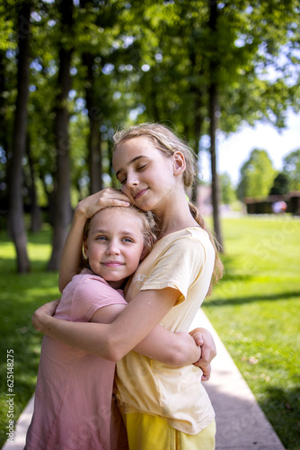 Two girls sisters of school age hug each other. A walk through the summer city park. Love and friendship within the family © evgeniia_1010