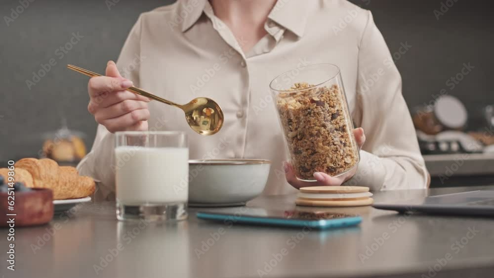 Cropped shot of unrecognizable woman using gold spoon while adding healthy granola into bowl with milk, having healthy breakfast at home Cropped shot of unrecognizable woman using gold spoon while adding healthy granola into bowl with milk, having healthy breakfast at home