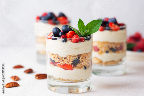 Fototapeta Vegan dessert in a glasses with berries, mint, nuts, whipped cream and biscuit