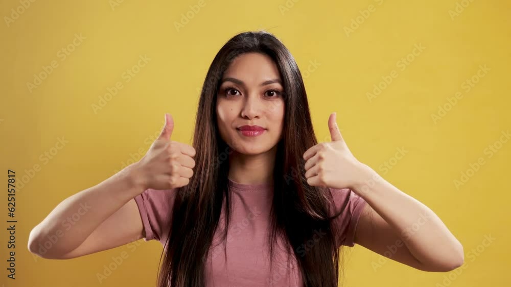 Asian Girl with a confident smile in a studio doing a thumbs-up gesture - extreme slow motion shot Asian Girl with a confident smile in a studio doing a thumbs-up gesture - extreme slow motion shot