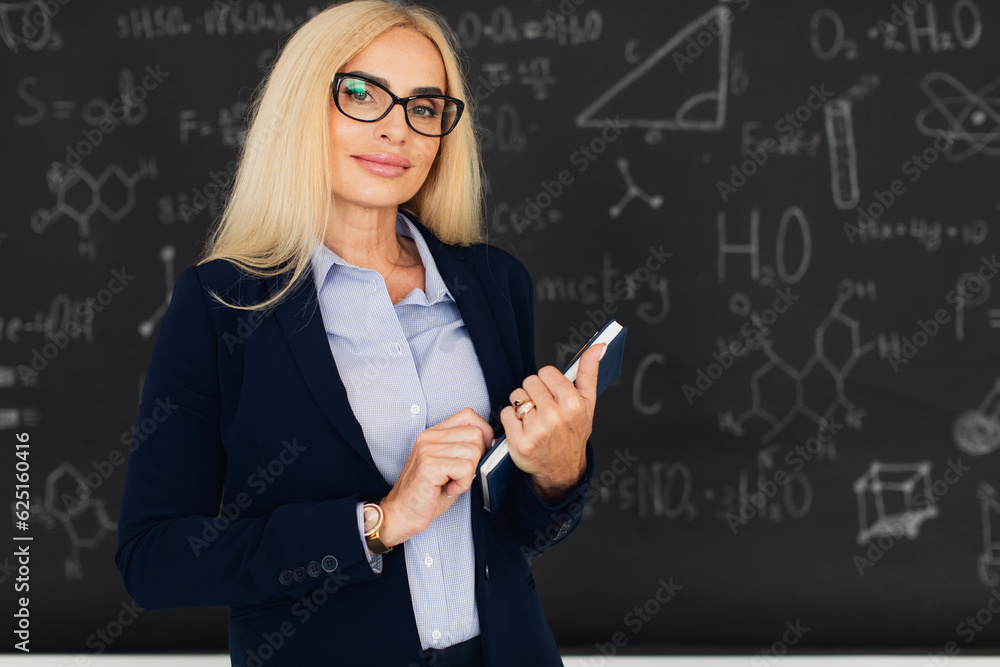 Portrait of happy blonde teacher woman standing near the blackboard in the classroom. Portrait of happy blonde teacher woman standing near the blackboard in the classroom.