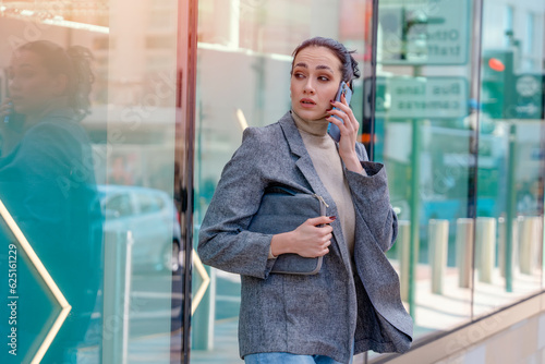 unhappy woman or student in a jacket and jeans crossing the road and talking on the phone