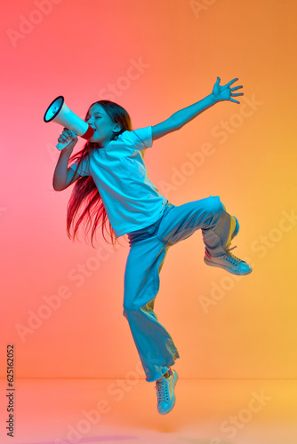 Active excited child wearing casual style clothes jumping high over neon light background. Concept of childhood, emotions, kids fashion