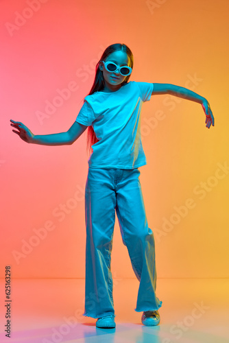 Portrait of cute school age girl, child wearing casual style clothes dancig over neon light background. Concept of childhood, music, fun photo