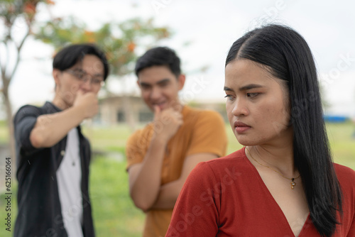 A young asian woman feels unsettled and annoyed after noticing two men checking out her body or catcalling. Sexual harassment and objectifying women. photo