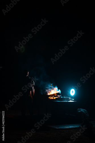 Man preparing bbq grill to cook on fire. Outside dark shot. Freeze moment of fire