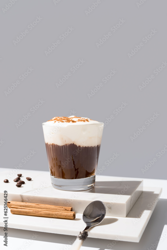 Verter crema batida en un café irlandés con canela sobre fondo gris Verter crema batida en un café irlandés con canela sobre fondo gris